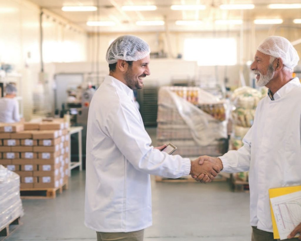 Two workers in a food manufacturing facility shake hands